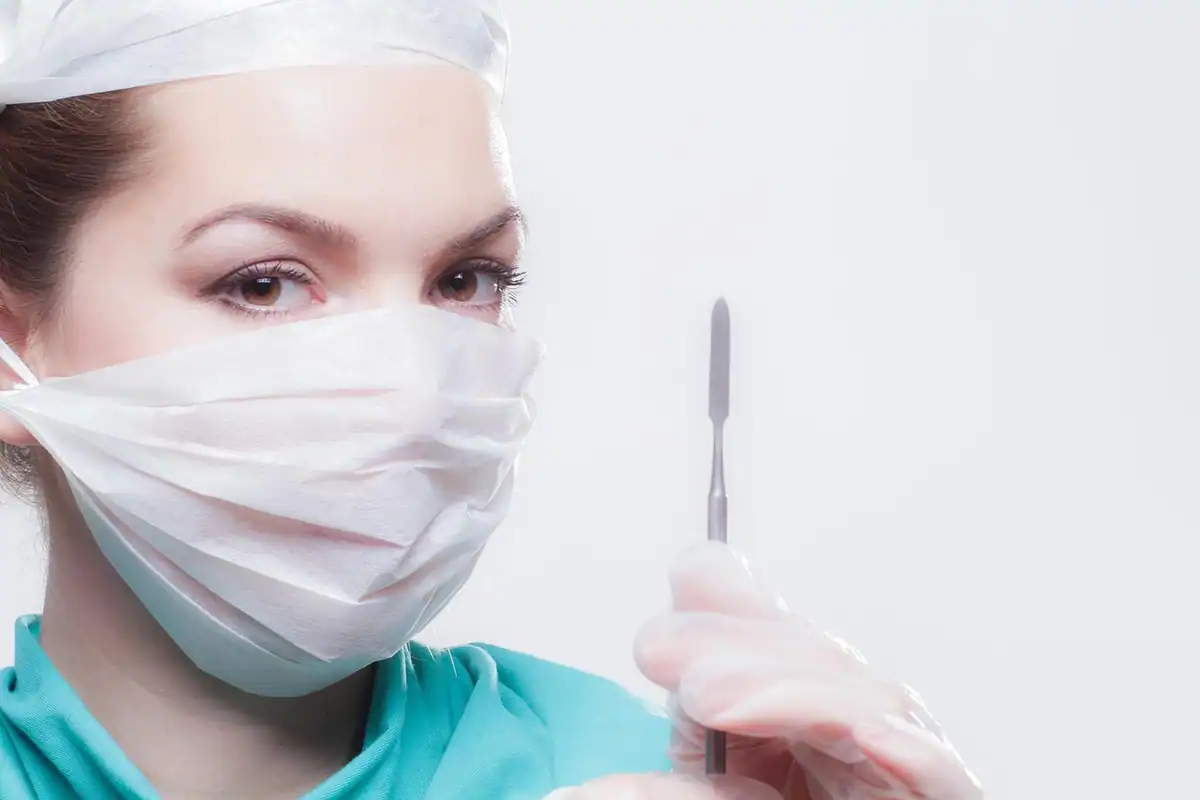 Chirurg cu mască medicală și bisturiu în mână, pregătit pentru o intervenție reconstructivă