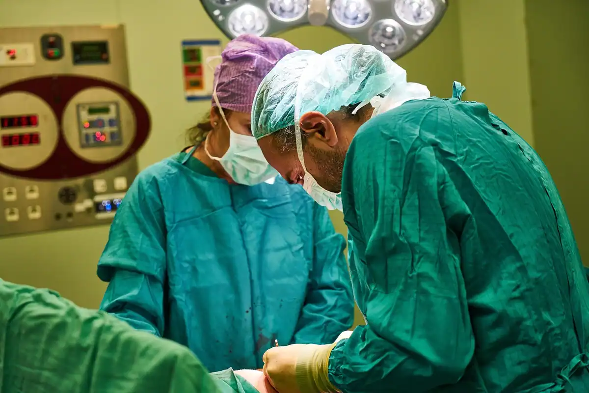 Echipă chirurgicală în halate verzi operează sub lămpile sălii de operație