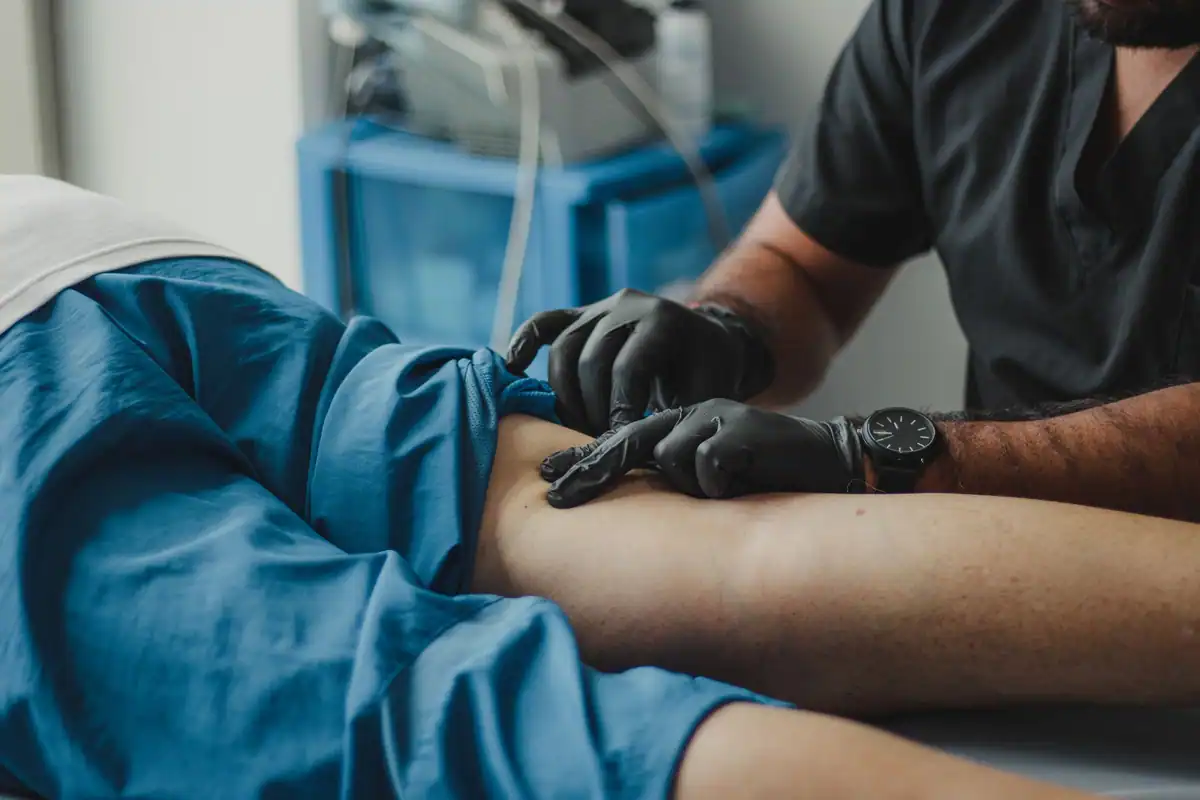 Medic cu mănuși negre examinează piciorul unui pacient, pentru a verifica circulația venoasă