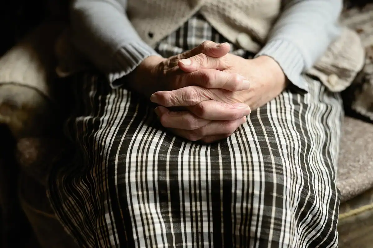 Mâinile încrucișate în poală ale unei femei în vârstă, care așteaptă liniștită