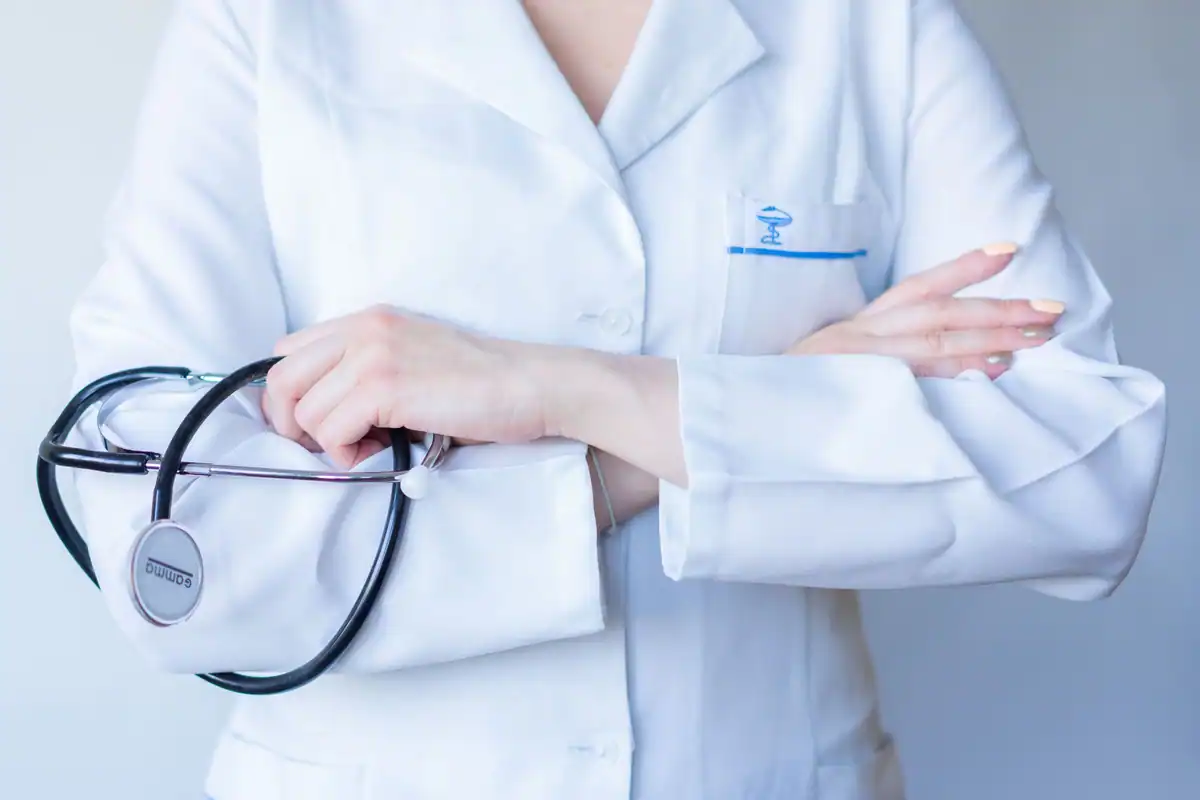 Medic în halat alb, cu brațele încrucișate și stetoscopul la gât, văzut din apropiere
