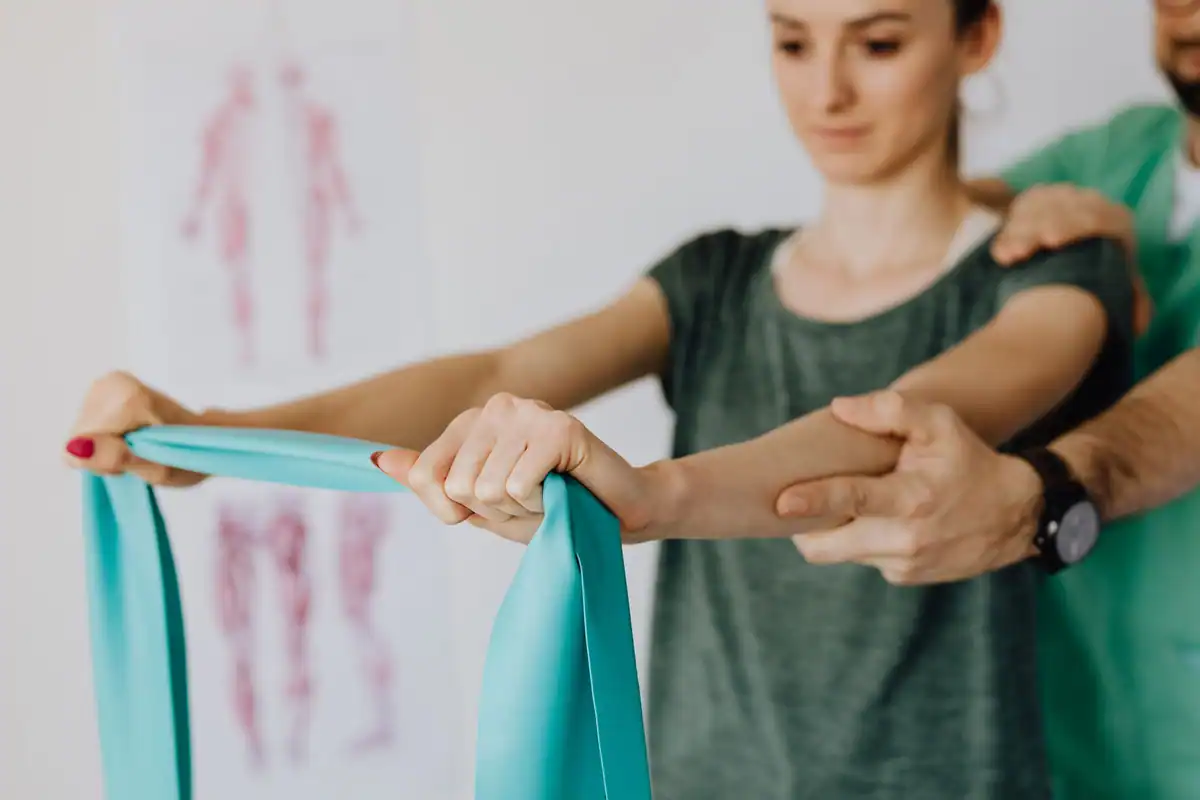 Specialist ajută o tânără să tragă o bandă elastică, într-un exercițiu de recuperare