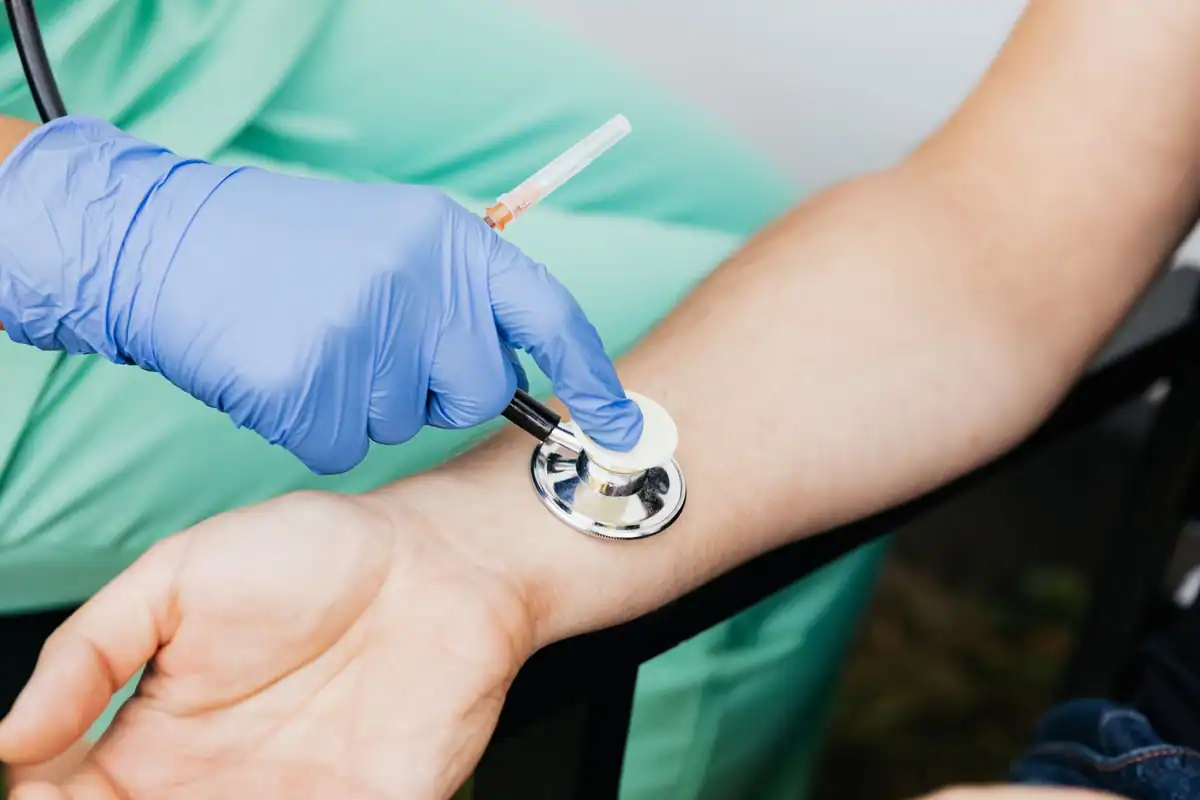 Medic cu mănuși verifică pulsul unui pacient la încheietura mâinii cu un stetoscop