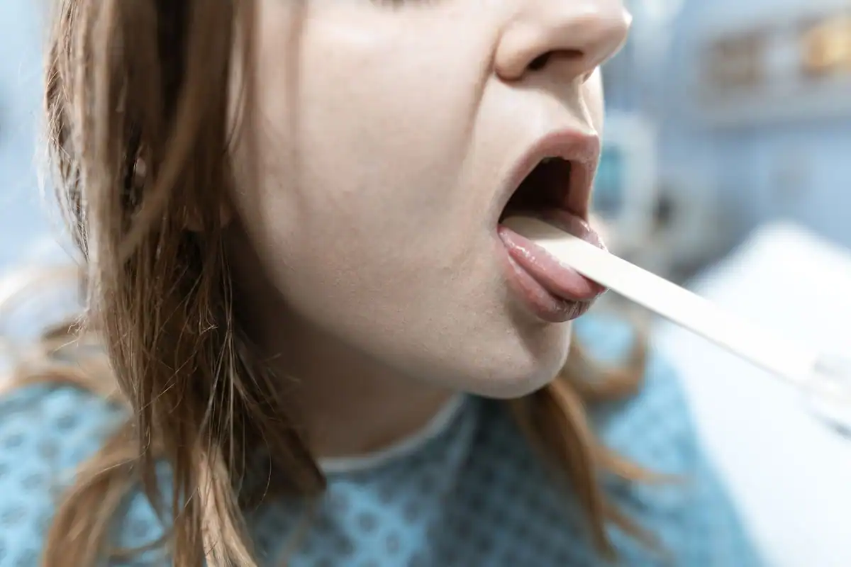 Pacientă cu gura deschisă, în timp ce medicul îi examinează gâtul cu o spatulă
