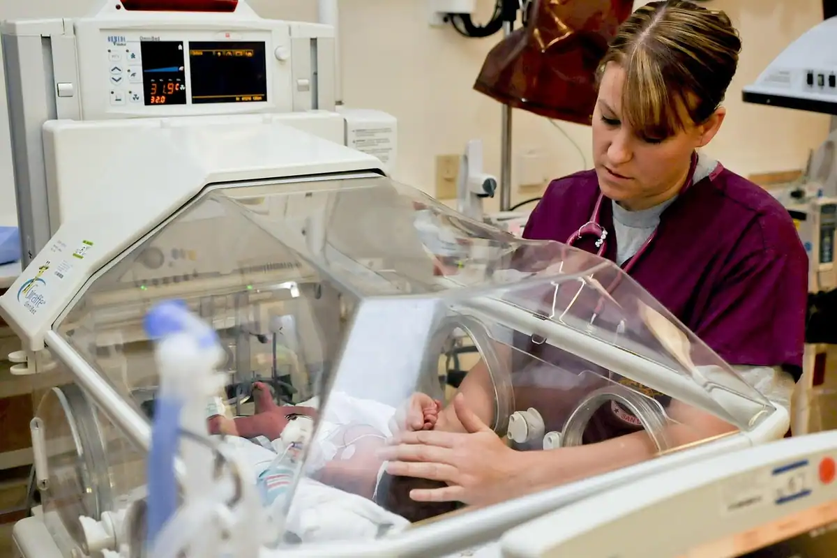 Asistentă se ocupă de un nou-născut într-un incubator transparent, într-o secție de neonatologie