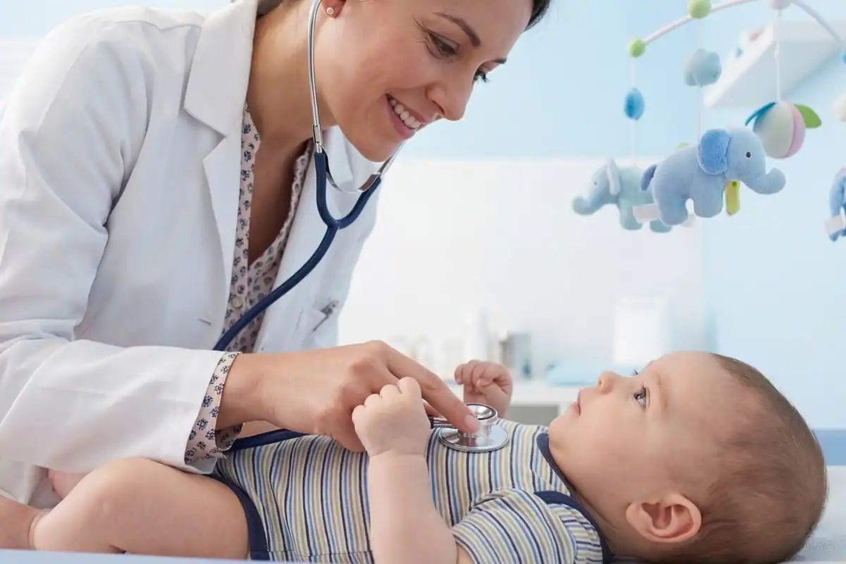 Pediatră zâmbitoare ascultă cu stetoscopul pieptul unui bebeluș culcat, într-un cabinet luminos